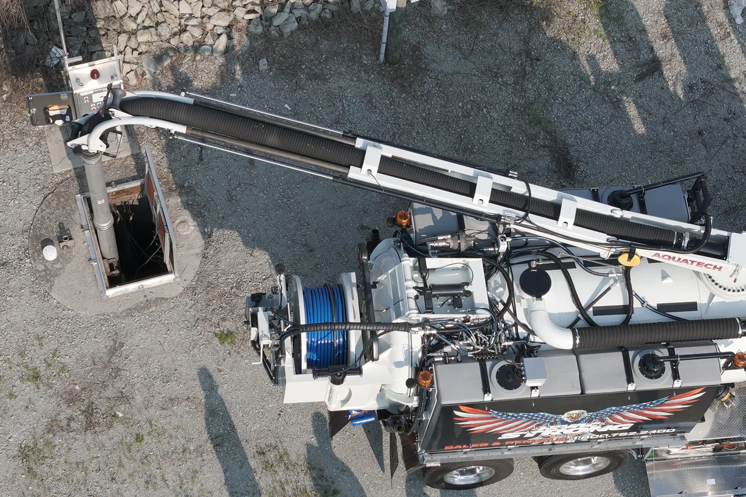 Aquatech combination sewer jetter in operation, cleaning a sewer with its hose extended into an open manhole on a gravel surface.
