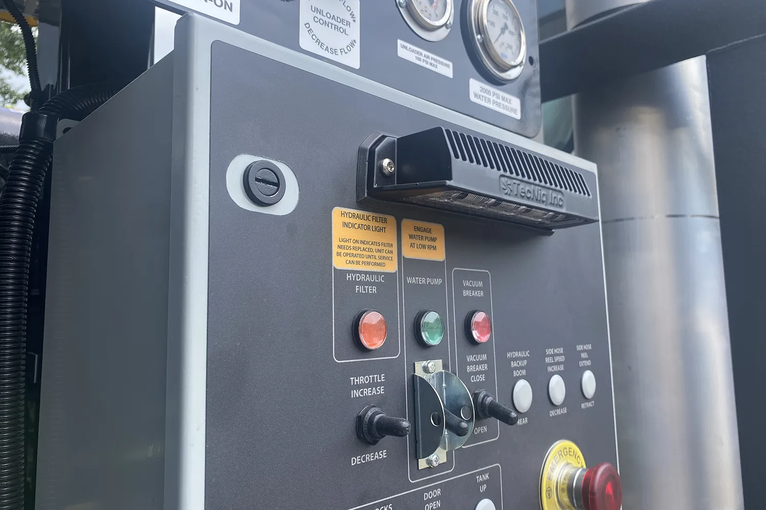 Aquatech sewer cleaning equipment control panel with gauges, hydraulic filter light, throttle controls, and emergency stop button.