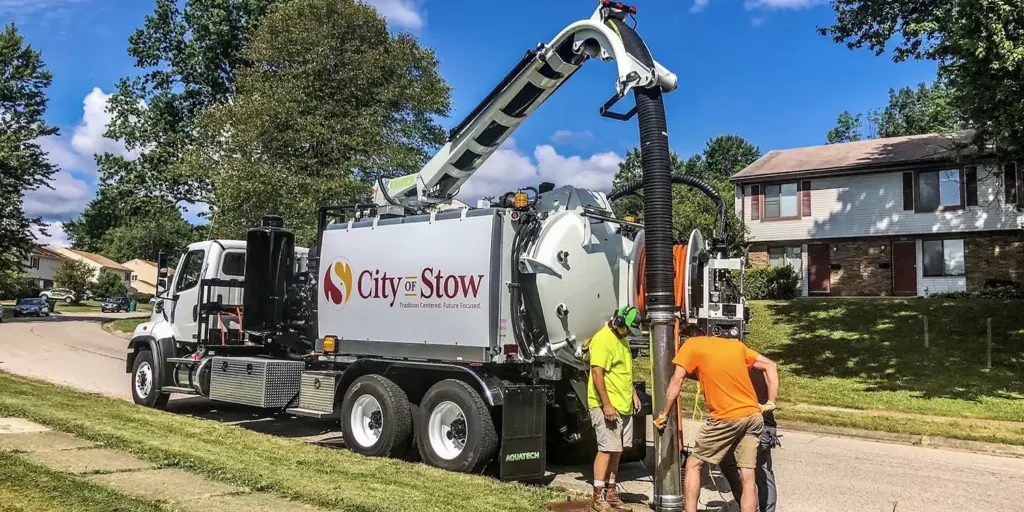 Aquatech combination sewer jetter in operation, labeled City of Stow, with operators working on sewer cleaning on a residential street.